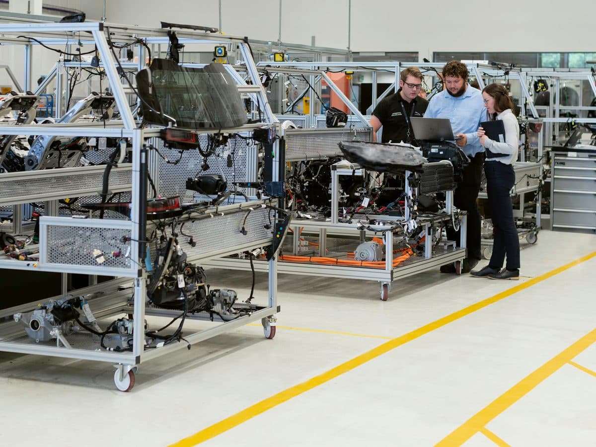 Three colleagues reviewing work at a laptop on an engineering assembly floor